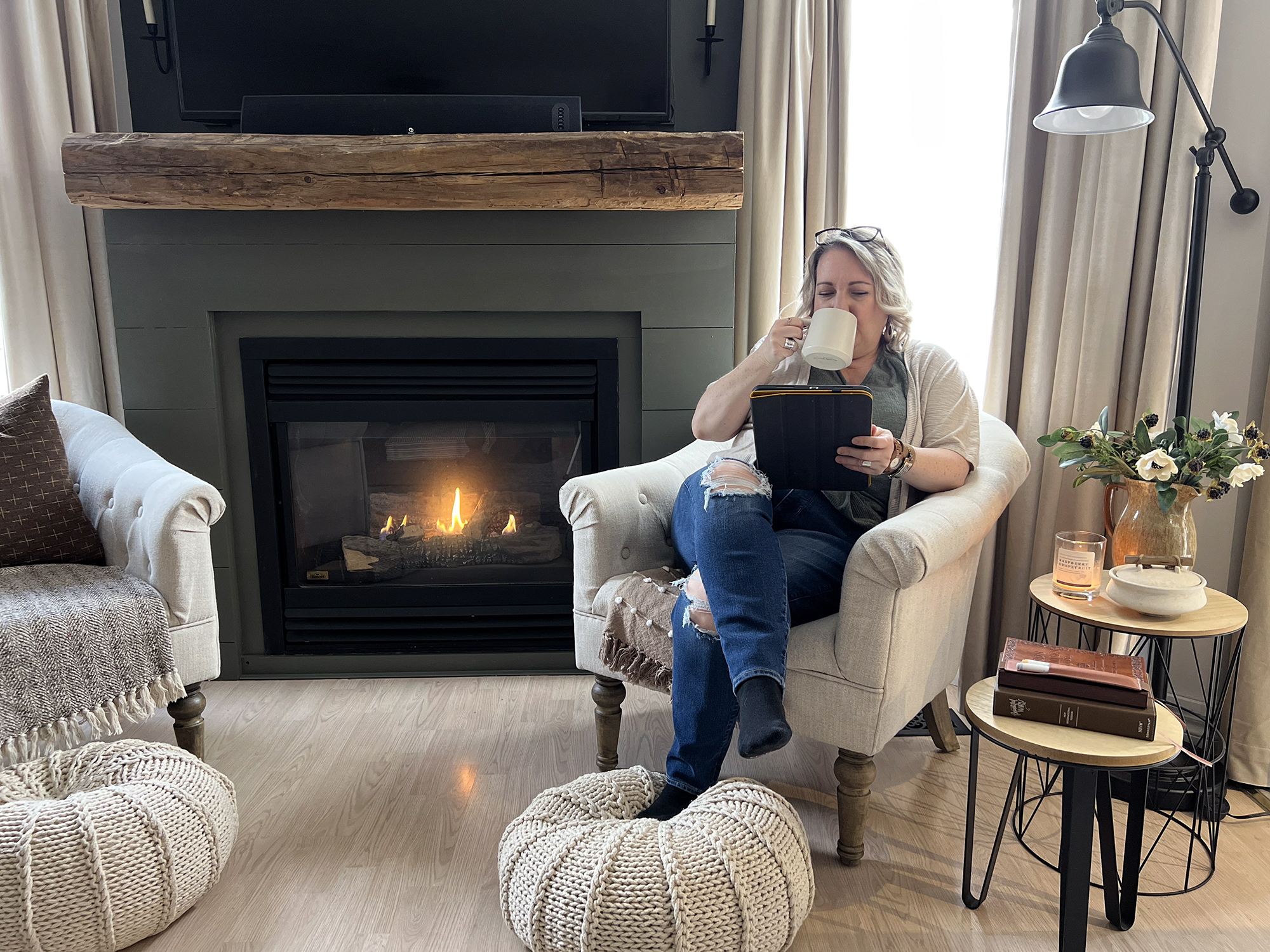 shannon sitting in chair by fireplace with ipad drinking coffee